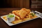 A pot of mushy peas on a plate with battered fish and chips.